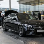 Chauffeur loading luggage into a black Mercedes at an airport terminal