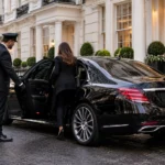 Chauffeur holding the rear door of a black Mercedes on a London Georgian street