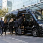 Conference delegates boarding a black executive minibus outside a modern venue